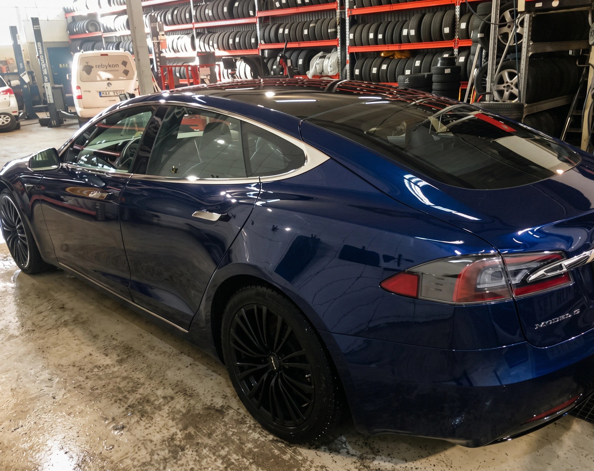 Mörkblå Tesla i verkstadshallen, med däckställ i bakgrunden